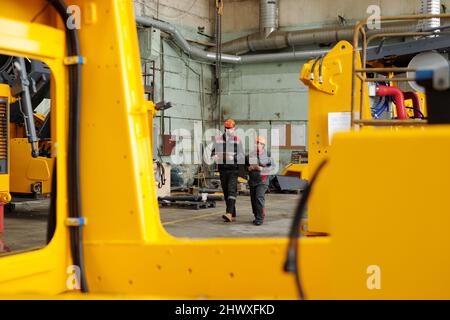 Two workers of large industrial plant moving along warehouse or workshop and consulting about technical points of new equipment Stock Photo