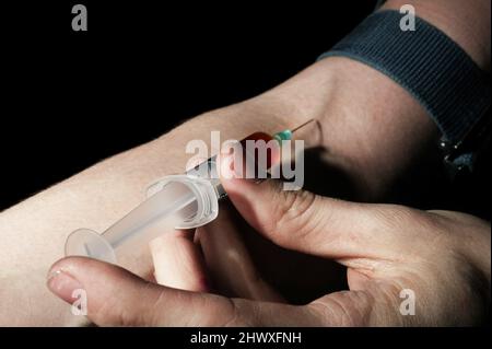 A heroin user injecting heroin into his arm. Heroin (diacetyl morphine) induces a psychological state of indifference immediately after it is taken. R Stock Photo