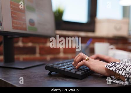 Close up of advertising agency employee hands typing on keyboard and working on research charts. Company office worker using computer to develop marketing strategy and business clients portfolio. Stock Photo
