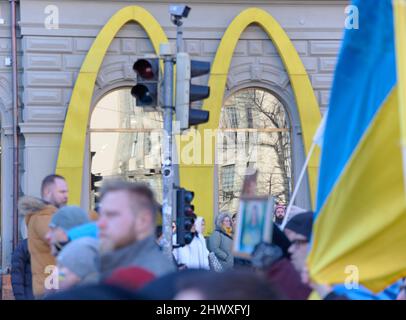 Helsinki, Finland - March 5, 2022: Yellow Mcdonald’s Golden Arches logo on the side of the building with a rally against Russia’s military actions and Stock Photo