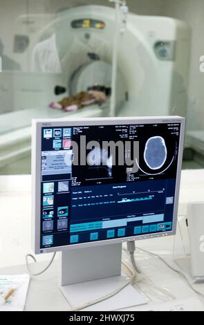 A patient undergoes a CT (Computer Tomography) scan  - Control screen of a CT scan (foreground) CT Scanner with patient (background) Stock Photo