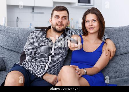 Young man and woman sitting on sofa at home watching TV Stock Photo