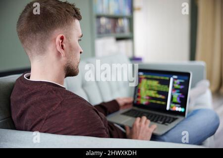 Rear View Of Young Man Relaxing. On Sofa Working From Home On Laptop Stock Photo