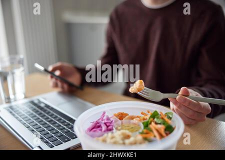Close Of Man Eating Healthy Lunch At Office Deak Whilst Using Laptop Stock Photo