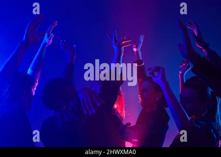 Minimal shot of diverse crowd dancing in club with hands up lit by neon lights Stock Photo