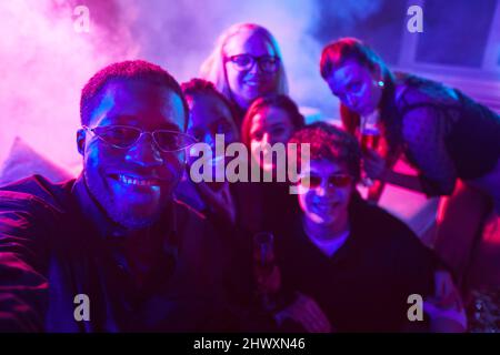 Portrait of African American man taking selfie with diverse group of friends at party in neon lights Stock Photo