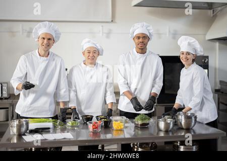 Portrait of young multiracial team of cooks preparing take away food in professional kitchen. Concept of dark kitchen for cooking for delivery. Idea of teamwork in a restaurant. Diverse people at job Stock Photo