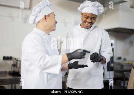 Asian and Latin chefs reading printed order while cooking meals in professional kitchen. Two chefs of different nationalities cook together in a restaurant Stock Photo