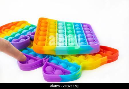 Anti-stress game Pop it. He presses multi-colored bubbles on a butterfly-shaped toy with his finger. Stock Photo