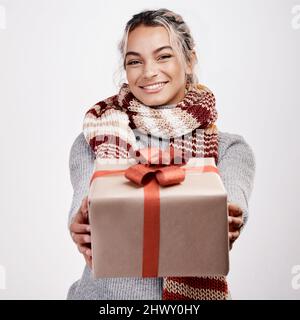 From me to you. Studio portrait of an attractive young woman handing you a gift while dressed in Christmas-themed attire. Stock Photo