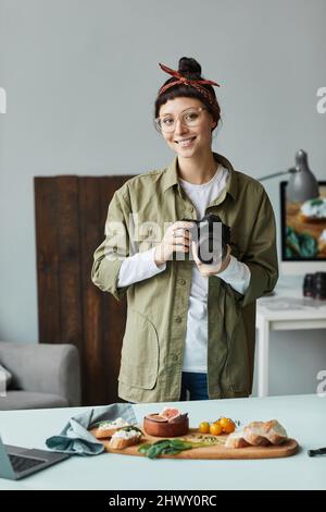 Vertical portrait of young female photographer smiling at camera while posing in studio Stock Photo