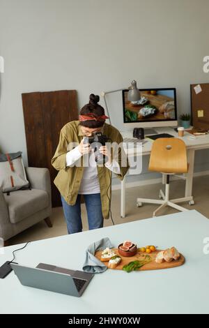 Vertical shot of female food photographer taking pictures while working in home studio Stock Photo