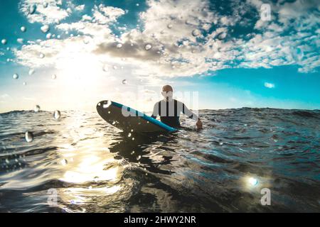 Surfer relaxing on surfboard at sunset in Tenerife waiting for the next good wave - Sport travel concept with shallow depth of field with drops on len Stock Photo