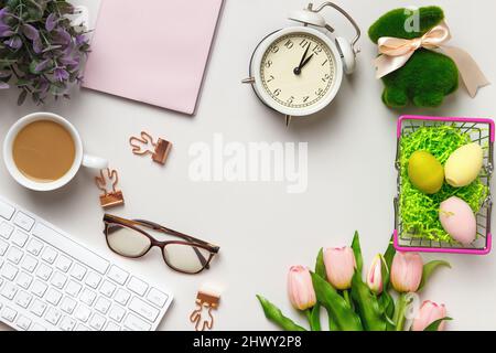 Desktop. Glasses coffee cup notepad on keyboard alarm clock on table with easter decorations. Stock Photo