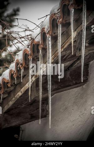 Large and sharp icicles hanging from a house roof Stock Photo