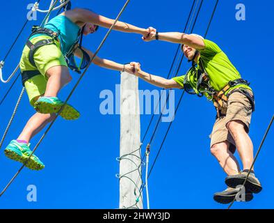 Two young people doing partner exercise in high ropes course Stock Photo