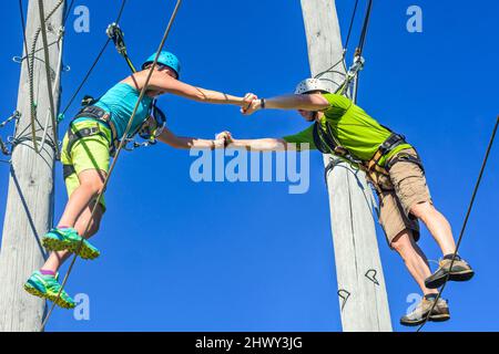 Two young people doing partner exercise in high ropes course Stock Photo