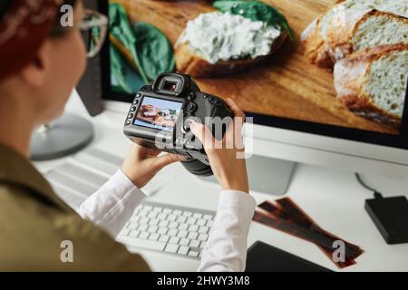 High angle view at female photographer holding camera with image on screen while editing photos at workplace Stock Photo