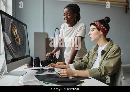 Portrait of two female photographers discussing images on computer screen while working on editing in studio Stock Photo
