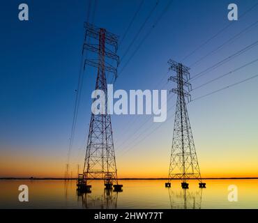 High voltage transmission lines crossing Wheeler Lake at dusk near Athens AL. Electricity pylons at sunset. Power and energy. Stock Photo