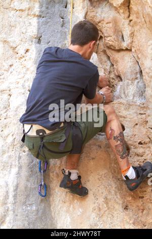 Rockstar of rock climbing. Rearview of a tattooed rock climber clinging onto a crack in the rockface. Stock Photo