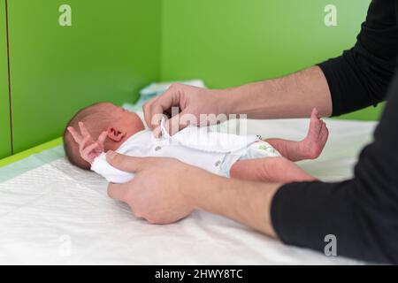 hands of a father who changes the diaper and puts a body on his newborn baby in the maternity hospital. paternity concept, baby care and new stage of Stock Photo