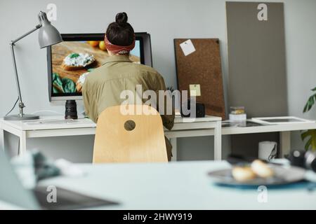 Back view of female food photographer using computer while retouching photos in studio, copy space Stock Photo