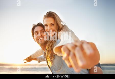 Celebrating their love. A blissful young couple celebrating their love on the seashore together. Stock Photo