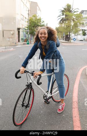 Full length portrait of cheerful african american young woman riding bicycle in city Stock Photo