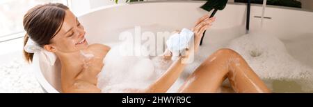 Lovely young woman bathing, using sponge and taking care of her skin, relaxing in the bathtub Stock Photo