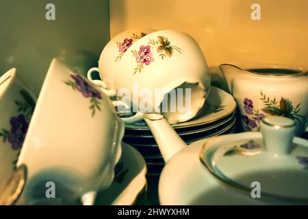a porcelain service with painted flowers lies in a closet on a shelf Stock Photo