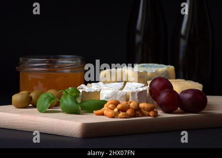 assorted sliced ​​cheeses, honey, nuts, olives, basil leaves stacked on a wooden board Stock Photo