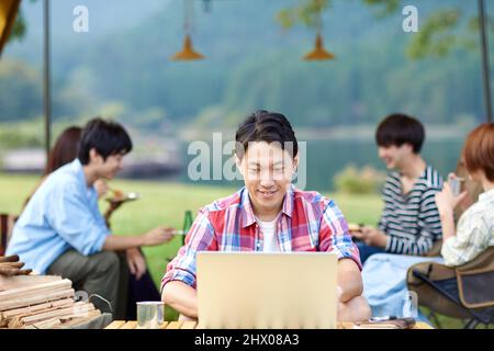 Japanese Men Teleworking At Campsite Stock Photo