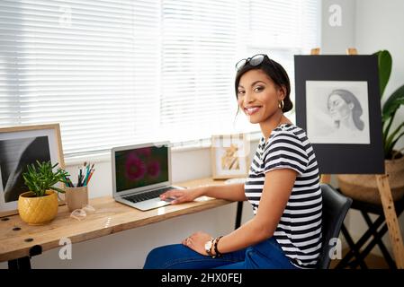 My art connects to many more people online. Portrait of an attractive young artist using a laptop while working inside her studio at home. Stock Photo