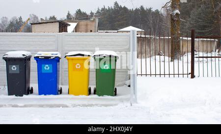 Four plastic trash cans near the fence in winter. The containers are located in the courtyard of the residential area. Separate waste sorting. Respons Stock Photo