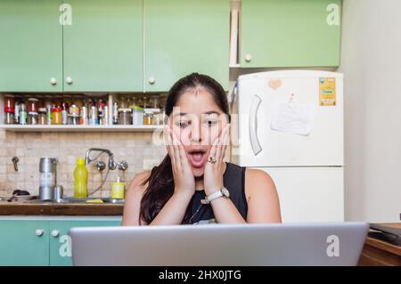 young caucasian venezuelan student woman at home watching the exam note on the computer surprised can't believe it, sitting in the living room of the Stock Photo