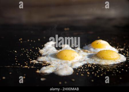 Three fried quail eggs on a hot flat top griddle. Pepper and oil steaming hot. Stock Photo