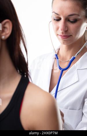 Doctor examining a female patient with a stethoscope listening to her lungs as she breathes in a close up cropped view of both people Stock Photo