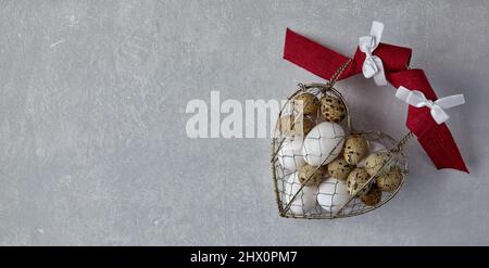 Chicken and quail eggs in a heart shaped woven metal wire basket Stock Photo