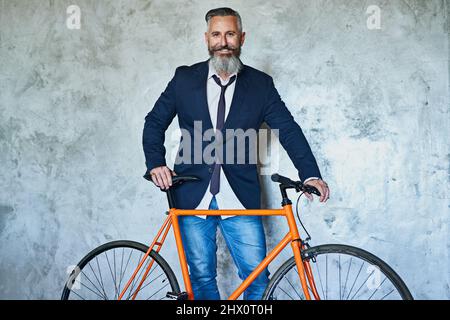 Off to go see the client. Studio shot of a confident middle aged businessman holding a red bicycle while standing against a grey background. Stock Photo