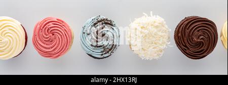 A row of decorated icing top cupcakes, against a light background. Stock Photo