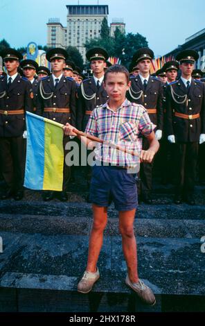 Young boy holding a Ukrainian Blue and Yellow flag in front of soldiers on Maidan square (Ukrainian: Майдан Незалежності) during a celebration of the first anniversary of Ukrainian independence in Kyiv, Ukraine, 1992. Stock Photo
