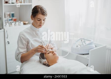 Cosmetologist making the Microdermabrasion procedure of the patient's face in spa salon. Medical treatment. Dermatology, cosmetology. Rejuvenation Stock Photo