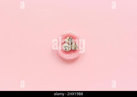 Three quail eggs in decorative pink nest in minimal style on pink paper background. Concept Happy Easter Greeting card Top view Copy space Template fo Stock Photo