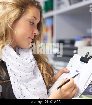 Stocking up on the right requirements. Cropped image of a pretty young woman in a shop making notes on a list. Stock Photo