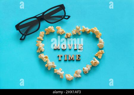 Popcorn in shape heart, 3D glasses, the text 'Movie time'. Still life on blue background. Flat lay, Top view.  Concept - love of cinema, lover of cine Stock Photo