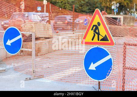 Repair work. Road repair in city street  in autumn. City street construction site with barricades, safety fence net, road work and detour signs. A clo Stock Photo