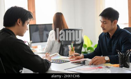 Two Asian male graphic designers are brainstorming and working together in the office open space. Stock Photo