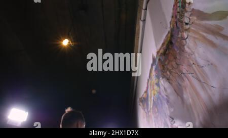 Artist designer draws an eagle on the wall. Craftsman decorator paints a picture with acrylic oil color. Painter painter dressed in a paint coat. Indoor. Dark magic cinematic look. Stock Photo