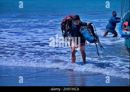 Wet landing on the beach in Costa Rica - man carrying tourist's backpacks, from the boat Stock Photo